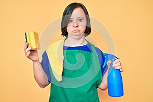 Brunette woman with down syndrome wearing apron holding scourer relaxed with serious expression on face