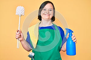 Brunette woman with down syndrome wearing apron holding scourer and toilet brush smiling with a happy and cool smile on face