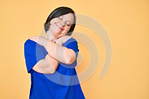 Brunette woman with down syndrome wearing casual clothes hugging oneself happy and positive, smiling confident