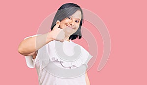 Brunette woman with down syndrome wearing casual white tshirt doing happy thumbs up gesture with hand