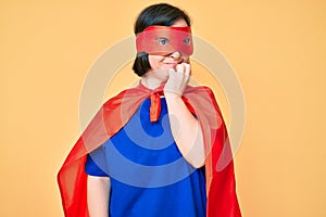 Brunette woman with down syndrome wearing super hero costume looking stressed and nervous with hands on mouth biting nails