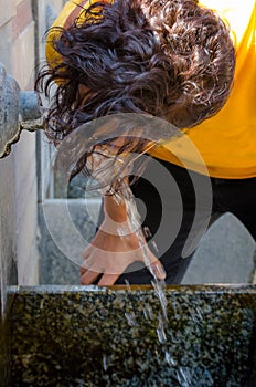 Brunette woman drinking water from the spout of a fountain