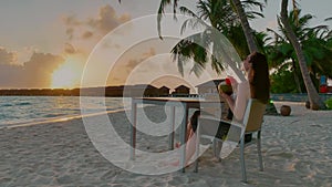 Brunette woman drinks coconut juice on beach at sunset