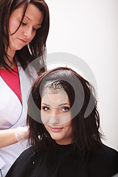 Brunette woman dying hair by hairstylist. In hairdressing studio.