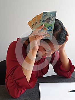 brunette woman with expression of despair and grabbing New Zealand money