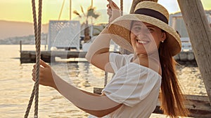 Brunette woman with flowing hair, dressed in a long white gown swaying on a beachside swing at sunset. Tourism