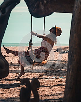 brunette woman with hat enjoying the beach on a swing