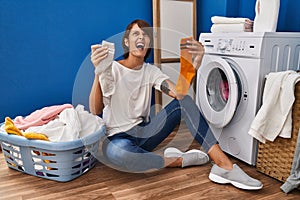 Brunette woman holding dirty socks angry and mad screaming frustrated and furious, shouting with anger looking up