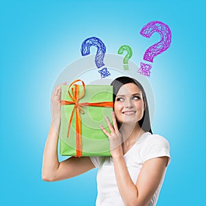 A brunette woman is holding a green gift box and question mark as a concept of gift uncertainty.