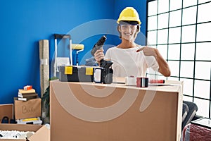 Brunette woman holding screwdriver at new home pointing finger to one self smiling happy and proud