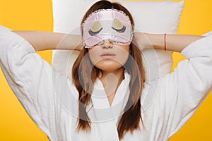 Brunette woman lies on pillow with sleeping mask over her eyes, relaxing