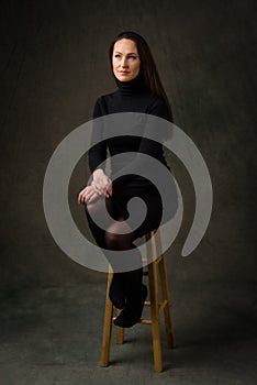 Brunette woman with long hair and black outfit siting on a stool