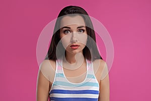 Brunette woman with long hair, dressed in colorful striped shirt, posing against pink studio background. Sincere