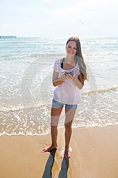 Brunette woman with long hair in shorts and light jacket on beach. Holds cherry in her hands. Sand.