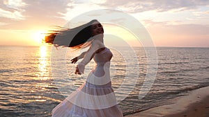 Brunette woman with long hair is spinning on the beach at sunset background