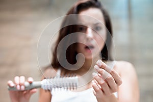 Brunette woman looking frightened when sees a lot of fallen hair on the brush hair loss problem