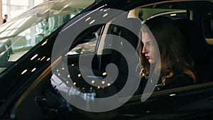 Brunette Woman in Luxury Car salon holding hands on steering wheel