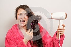 A brunette woman with matted hair dries it with a hair dryer. Hair care, overdried hair