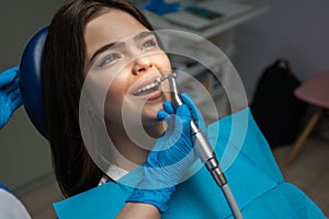 Brunette woman patient examined by dentist in blue gloves using dental mirror and scaler sitting in dental chair during teeth