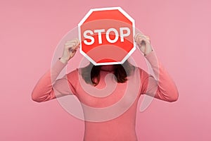 Brunette woman in pink sweater hiding face behind stop sign, way prohibited, stop violence