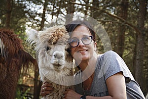 Brunette woman playing with cute alpacas at an eco farm in Poland