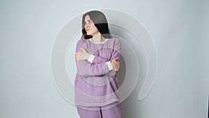 A brunette woman in purple warm pajamas hugs herself and enjoys the comfort of sleeping clothes