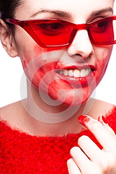 brunette woman in red glasses smears red lipstick on her face, red nails, white background