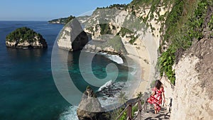 Brunette woman in a red long dress goes down on the stairs among rock and enjoying view of paradise the Diamond Beach