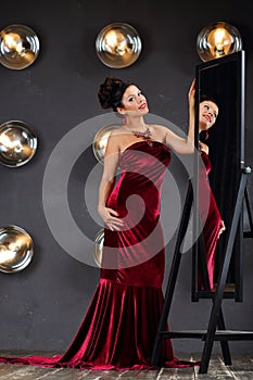 Brunette woman in red poses near mirror in studio