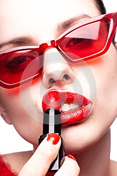 brunette woman in red sunglasses paints lips with red lipstick, red nails, white background