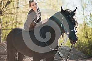 Brunette woman riding dark horse at summer green forest.