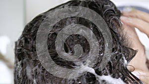 Brunette woman in shower washing her hair with shampoo close-up. Concept of cleanliness of hair and body, hygiene