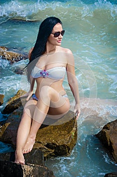 brunette woman sits on rocks at the seashor