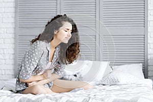 Brunette woman sitting on bed with menstruation pain