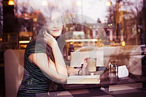 Brunette woman sitting at the cafe reading book, studing and drinking coffee and talking on the phone