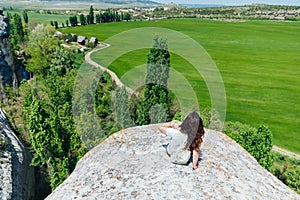 brunette woman sitting on a cliff looking at the nature of the journey