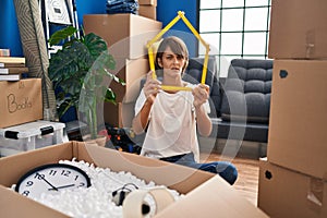 Brunette woman sitting on the floor at new home holding ruler clueless and confused expression