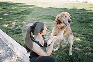 Brunette woman sitting on ground and holding paws of dog