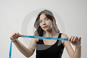 Brunette woman with slim body in black top on a diet looking in a camer and showing a blue centimeter tape. Healthy lifestyles