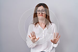 Brunette woman standing over white isolated background moving away hands palms showing refusal and denial with afraid and