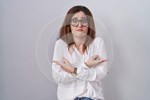 Brunette woman standing over white isolated background pointing to both sides with fingers, different direction disagree