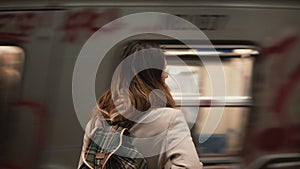 Brunette woman standing on railway station and waiting for her train. Girl in underground at evening looks on fast trams