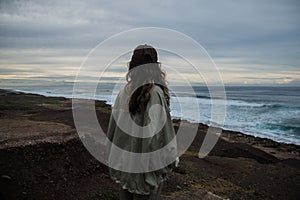 Brunette woman standing on a rocky seashore on a cloudy day