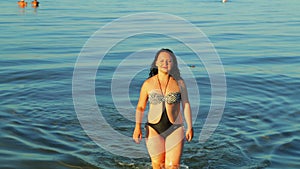 A brunette woman in a swimsuit comes out of the sea ashore