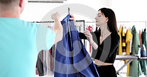 Brunette woman takes blue jacket hanging on rack from man