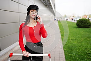 Brunette woman talking on mobile phone and holding shopping cart while standing outdoors