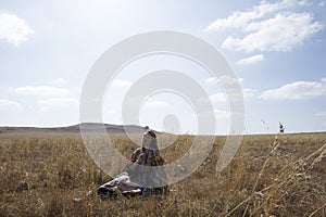 Brunette woman in tribal dress sitting in a field.