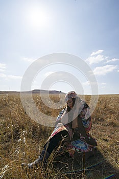 Brunette woman in tribal dress sitting in a field.