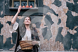 A brunette woman in vintage American wild West clothes sits under the window of a retro building with apples on the windowsill