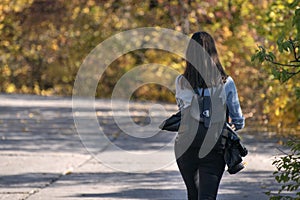Brunette woman walks along the alley of an autumn park. Lonely girl in the sunny forest. Back view